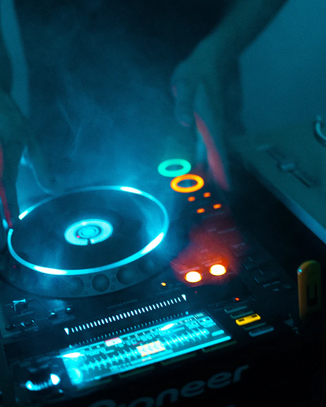 DJ hands on a CDJ deck glowing blue in the haze